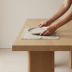 Hands setting a plate on the architectural teak dining table