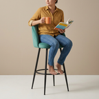 Person reading with a mug while seated on the teal bar stool
